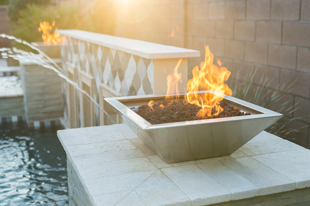 Fire bowl with flames on a poolside ledge at sunset