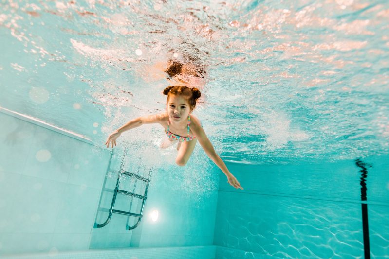 adorable kid swimming underwater in clear water in swimming pool
